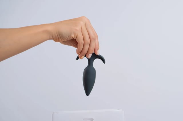 black-anal-plug-held-above-storage-box Black anal plug held above a white storage box