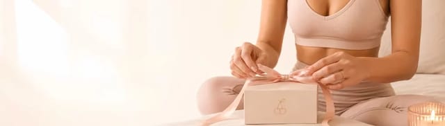blissfulcherry-signup-gift-box-yoga-banner Woman in blush yoga wear tying a ribbon on a BlissfulCherry gift box beside a lit candle.