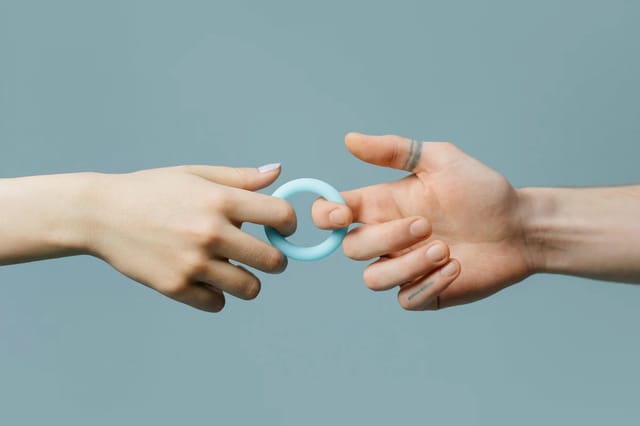 blue-ring-toy-hands-lifestyle Two hands holding a small blue ring-shaped intimate toy against a soft blue background.