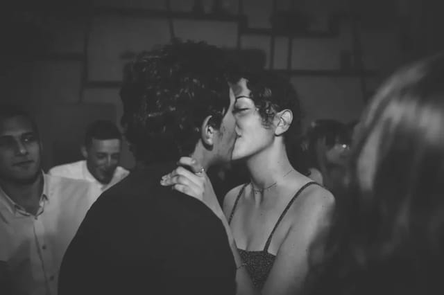 couple-kissing-at-nightlife-event Black-and-white photo of a couple kissing at a crowded nightlife event.