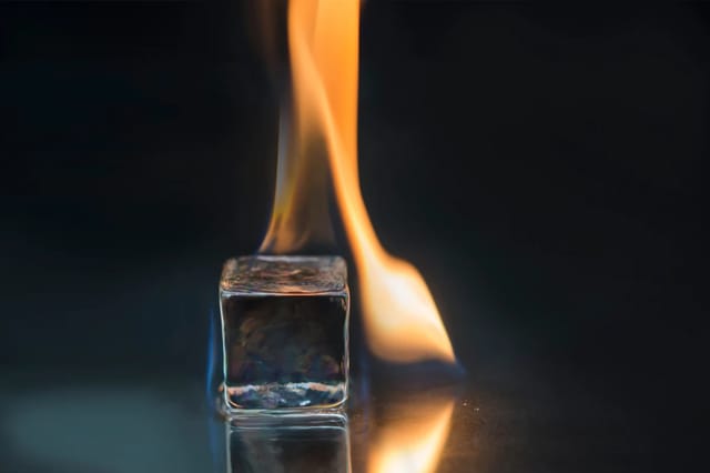 flame-and-ice-sensory-play-closeup Close-up of a flame beside an ice cube on a dark reflective surface.