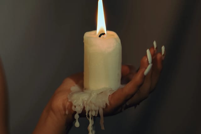 hand-holding-lit-candle-intimate-wellness Close-up of a hand holding a lit candle with melted wax in a dark, moody wellness setting.