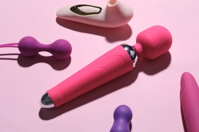 pink-intimate-toys-flat-lay-on-pink-background Flat lay of pink and purple intimate wellness toys on a soft pink background with dramatic shadows.