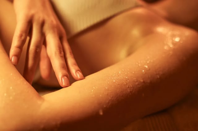 sensual-body-oil-massage-closeup Close-up of a woman applying oil to her leg in warm golden light for a sensual self-care scene.