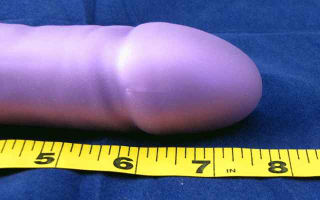 end of purple dildo lying next to measuring tape showing between 7 to 8 inches