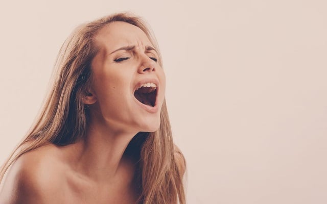 Blonde woman making intense orgasm face over light brown background