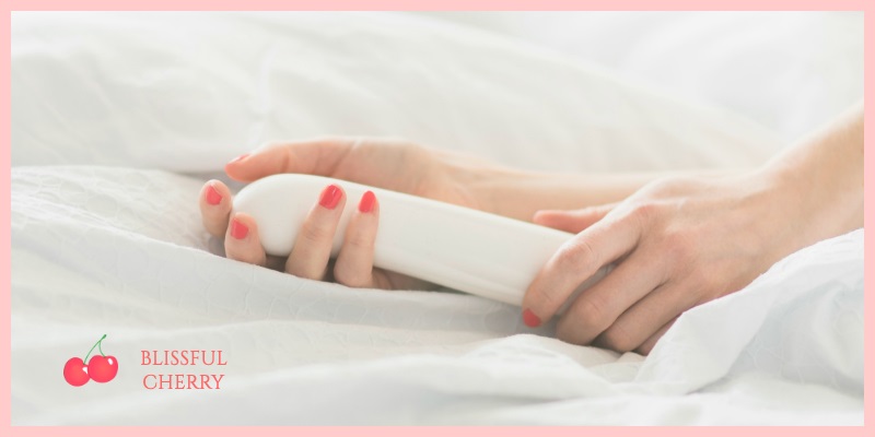 Hands of woman caressing a white vibrator in bed